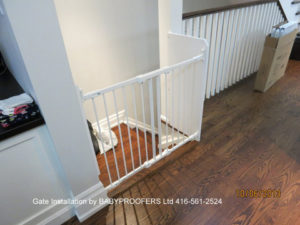 White baby gate installed at top of stairs where wall extends out.