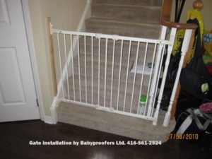 Typical white baby gate installed between wall and railing post.
