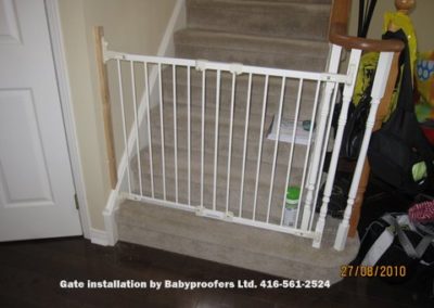 Typical white baby gate installed between wall and railing post.