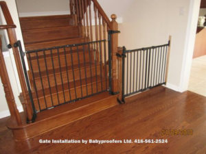 Dark green baby gates installed across two openings using newel post clamps.