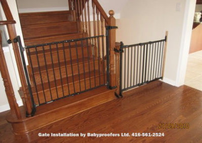 Dark green baby gates installed across two openings using newel post clamps.