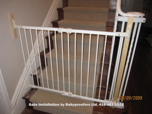 White baby gate attached to metal railings with special clamps.