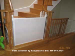 Retractable white baby gate installed at the bottom of the stairs between railings.
