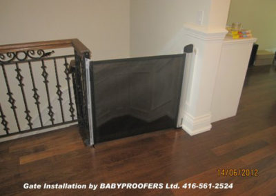 Retractable black baby gate installed at the top of some stairs.