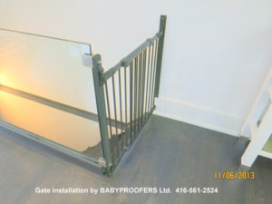 Baby gate installed between a glass rail and fixed wall.