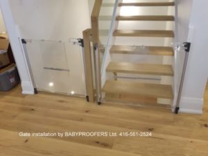 Two crystal clear baby gates installed at the junction of up and down stairs.