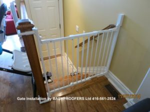White baby gate installed between wall and newel post without drilling hole in newel post.